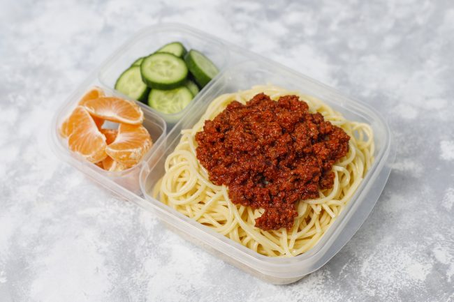 Takeaway spaghetti bolognaise in a plastic lunch box with detox