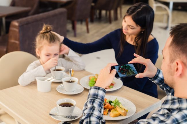leisure, technology, lifestyle and people concept – happy family with smartphone taking picture of food at restaurant