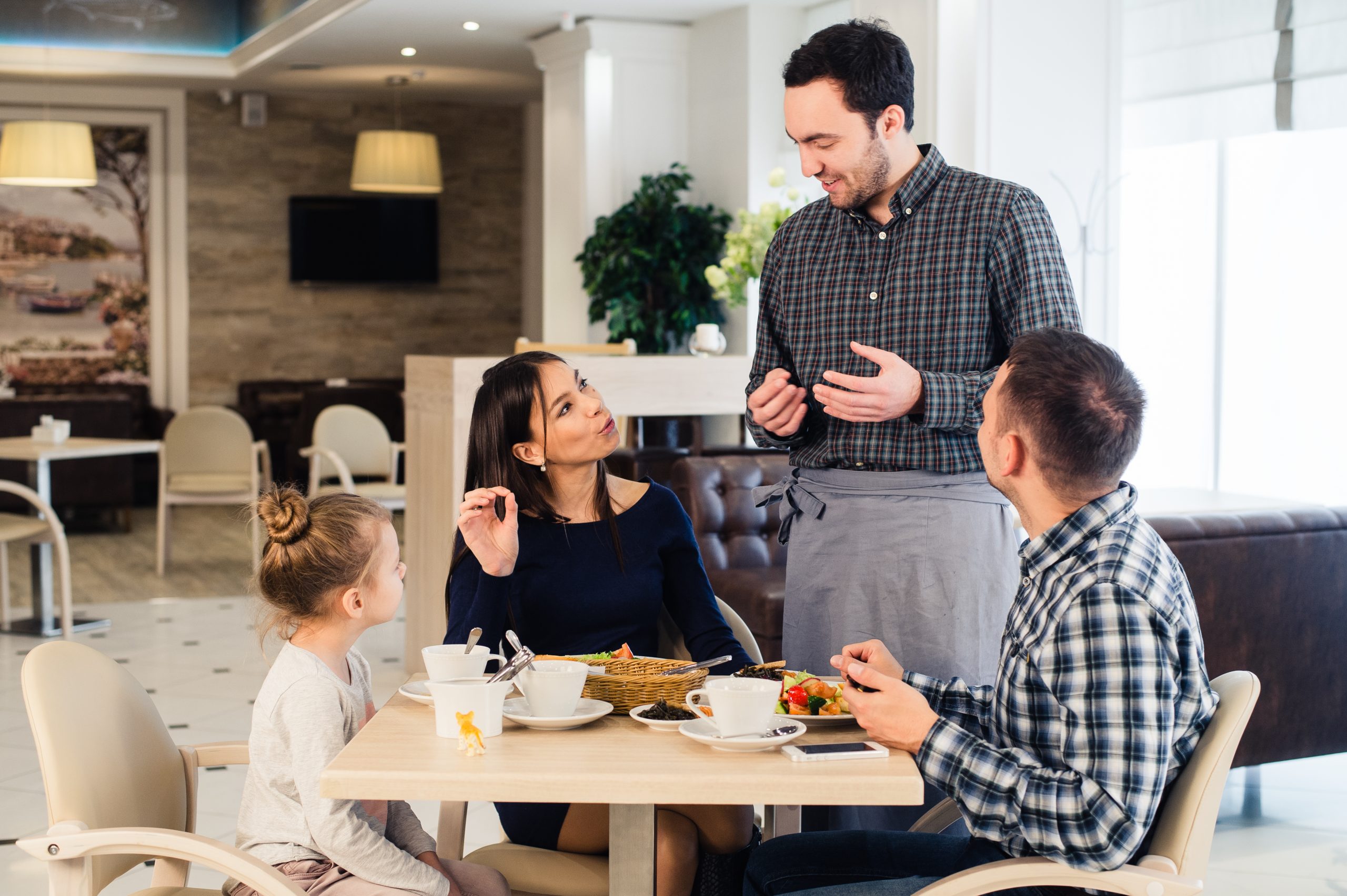Friendly smiling waiter taking order at table of family having dinner together